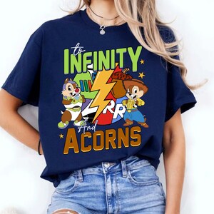 May include: A navy blue t-shirt featuring a graphic of Chip and Dale dressed as Buzz Lightyear and Woody from Toy Story. The text "to infinity and acorns" is printed on the shirt.