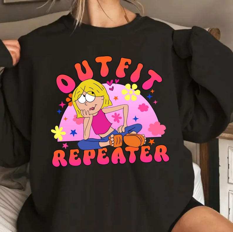 May include: A black crewneck sweatshirt featuring a graphic print of a cartoon character with blonde hair, a pink top, and blue pants. The text OUTFIT REPEATER is printed in pink and orange bubble letters above and below the character design.