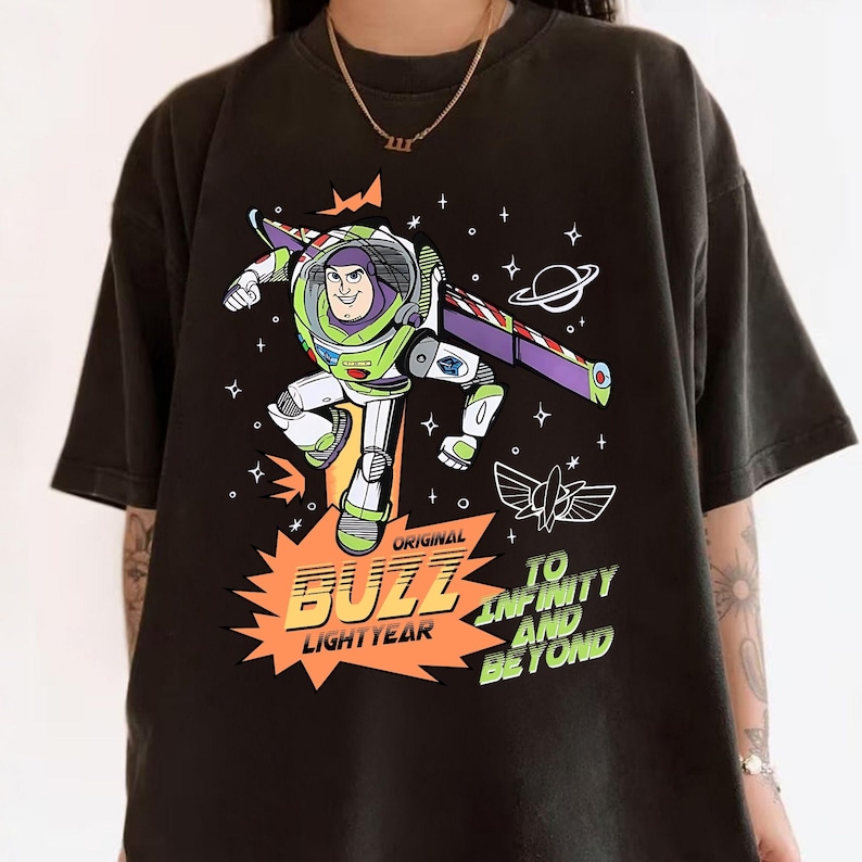 K&ouml;nnte beinhalten: Schwarzes T-Shirt mit einem farbenfrohen Buzz Lightyear-Motiv. Das Design enth&auml;lt die Worte "Original Buzz Lightyear" und "To Infinity and Beyond", sowie Sterne, einen Planeten und eine Rakete. L&auml;ssiger Stil.