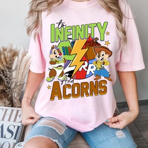 May include: Pink t-shirt featuring a graphic of cartoon characters, a lightning bolt, and the text "to infinity and acorns".