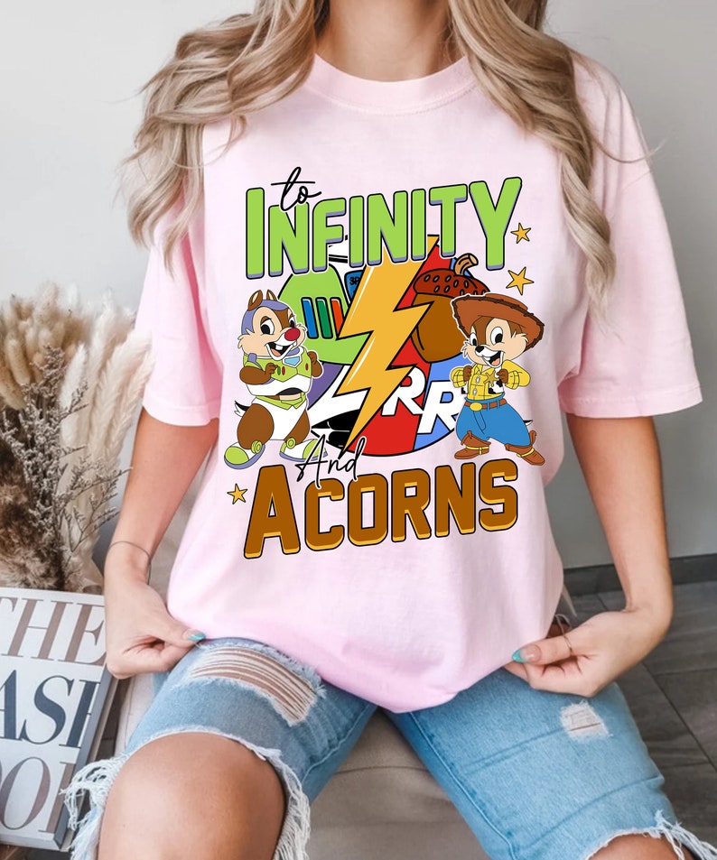 May include: Pink t-shirt featuring a graphic of cartoon characters, a lightning bolt, and the text "to infinity and acorns".