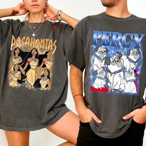 Pode incluir: Duas camisetas cinza carv&atilde;o. Uma apresenta a palavra "Pocahontas" acima de um gr&aacute;fico da personagem e outras mulheres. A outra camisa tem o nome "Percy" acima de um gr&aacute;fico de pugs. Ambas as camisas t&ecirc;m mangas curtas.