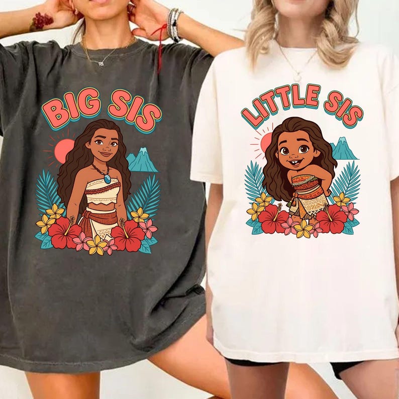 May include: Two t-shirts, one dark gray and one off-white, featuring a cartoon illustration of a girl surrounded by flowers and tropical leaves. The dark gray shirt says "BIG SIS" and the off-white shirt says "LITTLE SIS" in a colorful font.