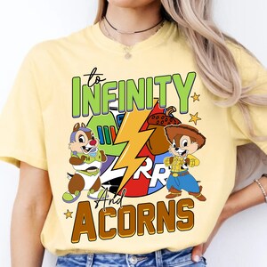 May include: Yellow t-shirt featuring a cartoon image of Chip 'n Dale. The shirt has the text "to infinity and acorns" with a lightning bolt graphic.