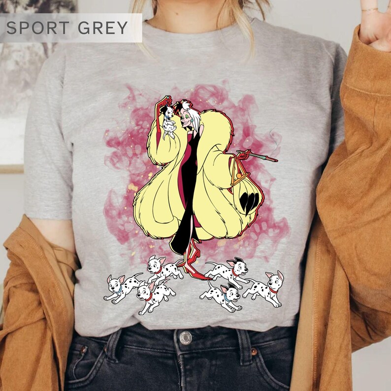 K&ouml;nnte beinhalten: Sportgraues T-Shirt mit einer Cartoon-Illustration einer Figur in einem gelben Mantel, einem schwarzen Kleid und roten Schuhen, die einen kleinen Hund und eine Tasche h&auml;lt, umgeben von laufenden Dalmatiner-Welpen. Der Text "SPORT GREY" steht oben.