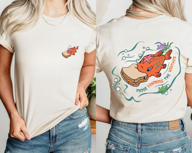 May include: A white t-shirt with a cartoon illustration of a fish eating a peanut butter and jelly sandwich. The text "Pudge Controls the Weather" is printed on the shirt.