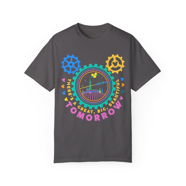 May include: A dark grey short-sleeve t-shirt featuring a colourful graphic of gears and a futuristic building. The text reads, "THERE'S A GREAT, BIG, BEAUTIFUL TOMORROW" in a circular arrangement around the central illustration with small mouse icons.