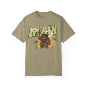 Puede incluir: Una camiseta color caqui con un estampado gr&aacute;fico de Maui de la pel&iacute;cula de Disney Moana. El gr&aacute;fico muestra a Maui sosteniendo su anzuelo de pesca y el texto "You're welcome Maui".