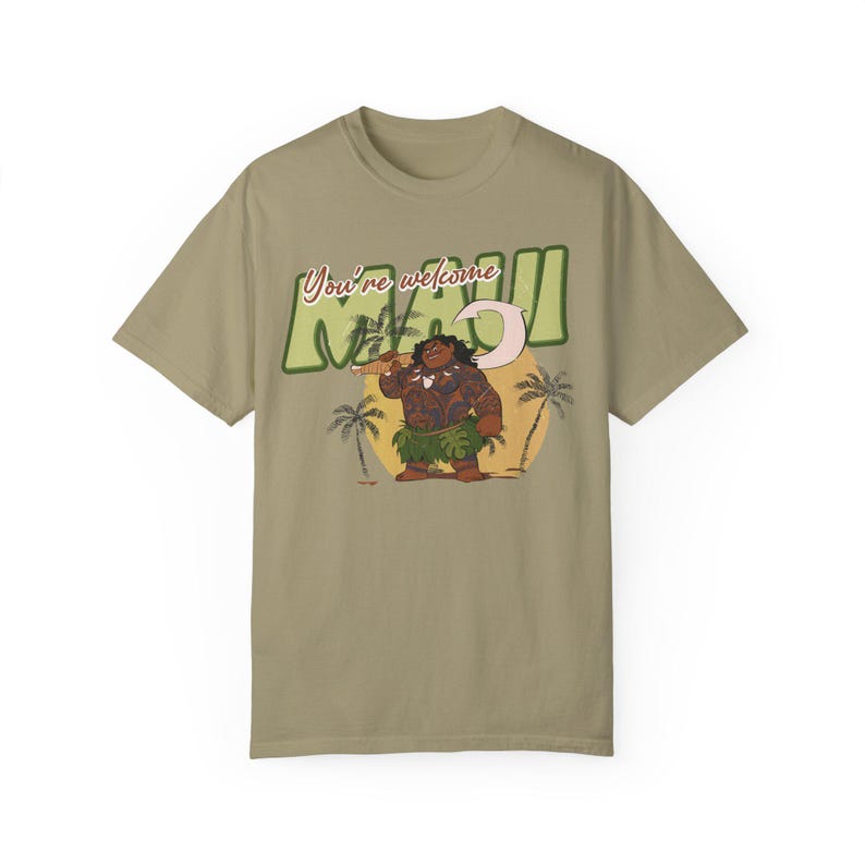 Puede incluir: Una camiseta color caqui con un estampado gr&aacute;fico de Maui de la pel&iacute;cula de Disney Moana. El gr&aacute;fico muestra a Maui sosteniendo su anzuelo de pesca y el texto "You're welcome Maui".