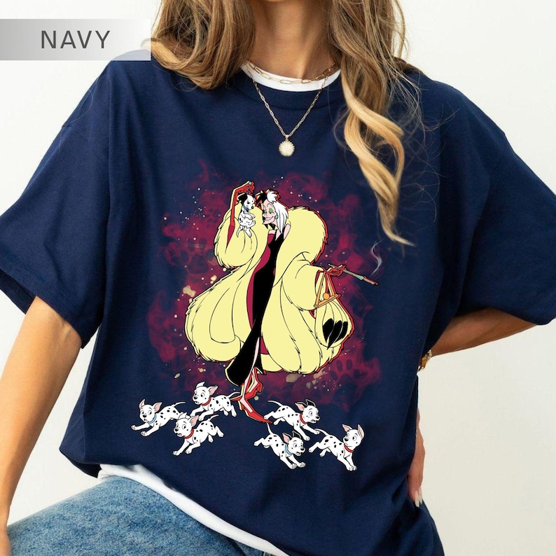 K&ouml;nnte beinhalten: Marineblaues T-Shirt mit einer Cartoon-Illustration einer Figur in einem gelben Mantel, die eine Zigarette und eine Tasche h&auml;lt, umgeben von Dalmatiner-Welpen. Das T-Shirt hat einen wei&szlig;en Kragen und eine goldene Halskette.