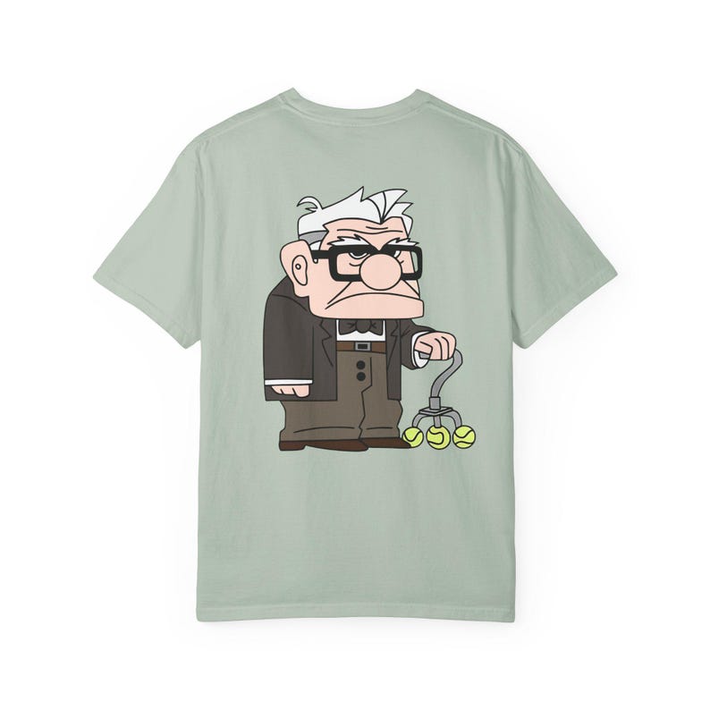 May include: A light green t-shirt featuring a cartoon illustration of an elderly man with glasses, a suit, and a cane with tennis balls. The character is from the animated movie "Up".
