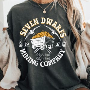 May include: A black t-shirt with a white graphic design of a mining cart filled with gold nuggets. The graphic also includes the text "Seven Dwarfs Mining Company", "Heigh ho! Heigh ho!" and the numbers "19" and "37".