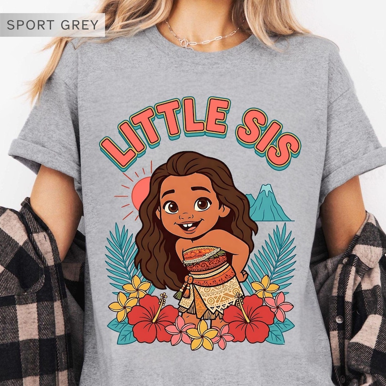 May include: Sport grey t-shirt with a colorful graphic of a cartoon character and the text "LITTLE SIS". The design includes a sun, mountain, and tropical flowers. The shirt is a crew neck.