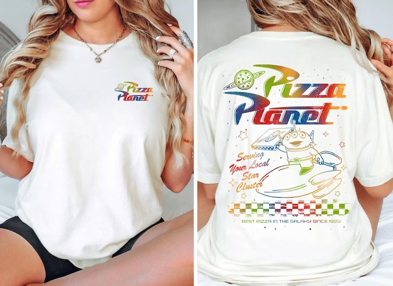 Puede incluir: Una camiseta blanca con un gr&aacute;fico de arco&iacute;ris del logotipo de Pizza Planet y un personaje de dibujos animados que sostiene una caja de pizza. El texto en la camiseta dice "Pizza Planet", "Serving Your Local Star Cluster" y "Best Pizza in the Galaxy Since 1995".