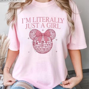 May include: Light pink t-shirt with the text "I'M LITERALLY JUST A GIRL" in pink. The design features a disco ball Mickey Mouse head with a pink bow. The word "BLOSSOM" is in the top left corner.