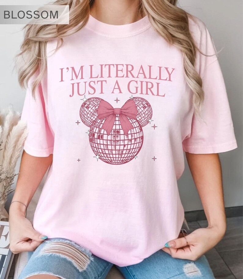May include: Light pink t-shirt with the text "I'M LITERALLY JUST A GIRL" in pink. The design features a disco ball Mickey Mouse head with a pink bow. The word "BLOSSOM" is in the top left corner.