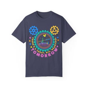 May include: A dark blue short-sleeve t-shirt featuring a colourful graphic of a gear-shaped design with the text "THERE'S A GREAT, BIG, BEAUTIFUL TOMORROW" surrounding a central illustration of a futuristic building and a rocket ship.