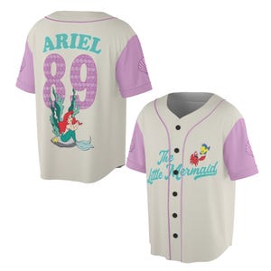May include: Cream-colored baseball jersey with light purple sleeves and accents. The back features the name "ARIEL" and the number "89" in a purple scale pattern, along with a cartoon image of Ariel. The front displays "The Little Mermaid" text and character graphics.