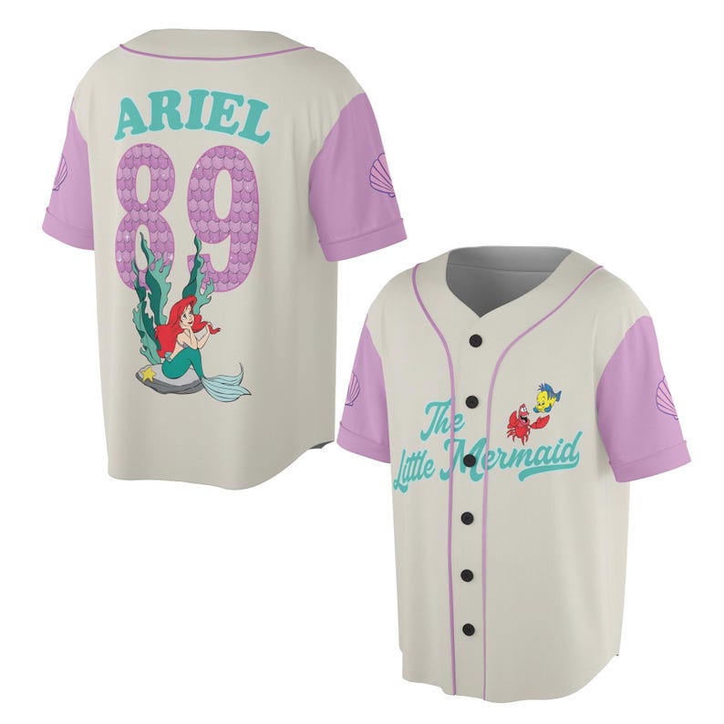 May include: Cream-colored baseball jersey with light purple sleeves and accents. The back features the name "ARIEL" and the number "89" in a purple scale pattern, along with a cartoon image of Ariel. The front displays "The Little Mermaid" text and character graphics.