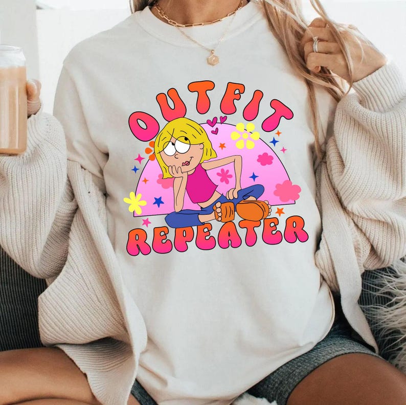 May include: A cream-colored crewneck sweatshirt featuring a graphic print of a cartoon character with blonde hair wearing a pink top and blue pants. The text OUTFIT REPEATER is printed in bold pink letters above and below the character illustration.