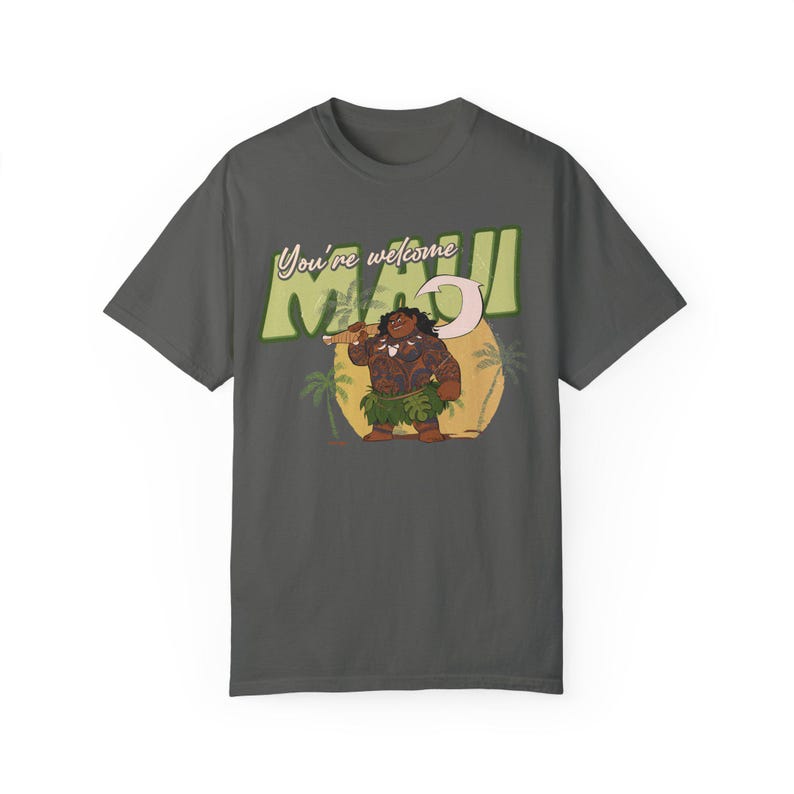 Puede incluir: Una camiseta gris oscuro con una imagen de dibujos animados de Maui de la pel&iacute;cula Moana. El texto "You're welcome Maui" est&aacute; impreso en la camiseta en un estilo retro.