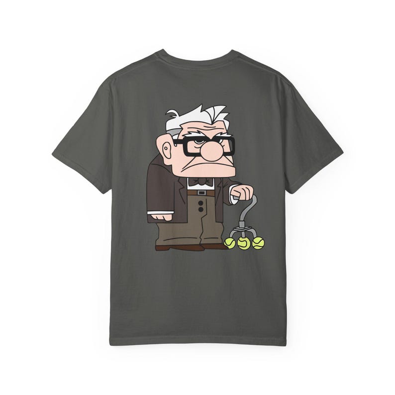 May include: Dark gray t-shirt featuring a cartoon illustration of an elderly man with glasses, a bow tie, and a cane with tennis balls. The character is wearing a brown suit jacket and pants. The design is centered on the shirt.