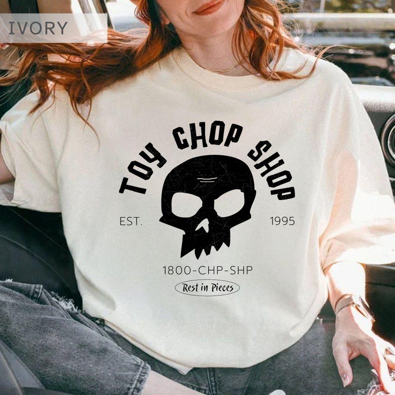 Pu&ograve; includere: Una t-shirt color avorio con una grafica nera di un teschio centrata sul petto. Il testo recita TOY CHOP SHOP, EST. 1995, 1800-CHP-SHP e Rest in Pieces. Il design &egrave; stampato in un carattere grassetto senza grazie con una texture usurata.