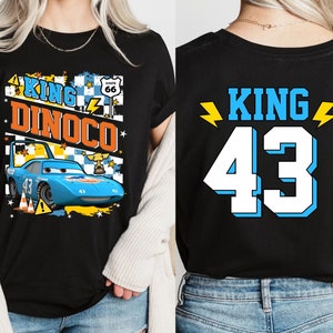 May include: Black t-shirt with a blue car graphic and the text "King Dinoco" on the front. The back of the shirt has the text "King 43" in yellow and blue.