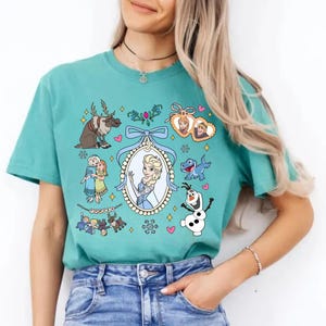 Puede incluir: Camiseta turquesa con un gr&aacute;fico colorido de personajes de la pel&iacute;cula animada "Frozen". El dise&ntilde;o incluye im&aacute;genes de Elsa, Anna, Olaf, Sven y otros elementos de la pel&iacute;cula, rodeados de corazones y copos de nieve.