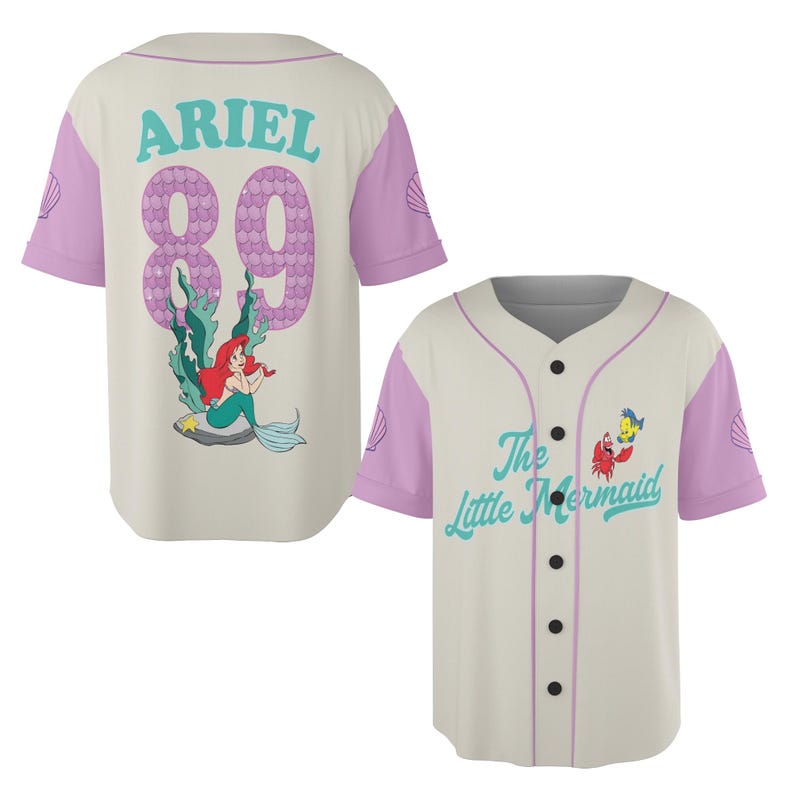 May include: Cream-colored baseball jersey with light purple sleeves and accents. The back features the name "ARIEL" above the number "89" in a purple bubble font, with an illustration of Ariel. The front displays "The Little Mermaid" and character art.