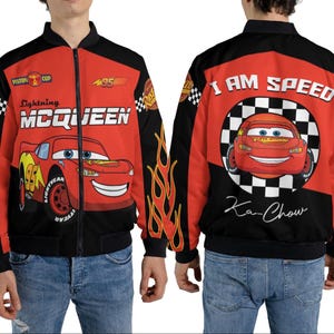 May include: A red and black Lightning McQueen bomber jacket. The front features the character's name and image, while the back displays "I AM SPEED" and "Ka-Chow." Flames adorn the sleeves. The jacket is worn by a person.