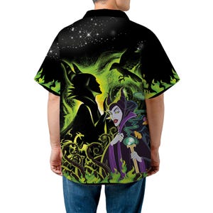 Op de afbeelding: Zwart overhemd met knopen met een levendige afbeelding van een schurkachtig personage met groene en paarse accenten. Het ontwerp omvat een silhouet, een raaf en een staf, tegen een donkere, sterrenhemel achtergrond. Het shirt heeft korte mouwen.