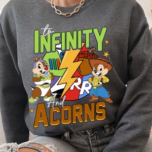 May include: Grey sweatshirt featuring a cartoon graphic of two chipmunks, one dressed as a space ranger and the other as a cowboy. The text "to infinity and acorns" is printed on the sweatshirt.