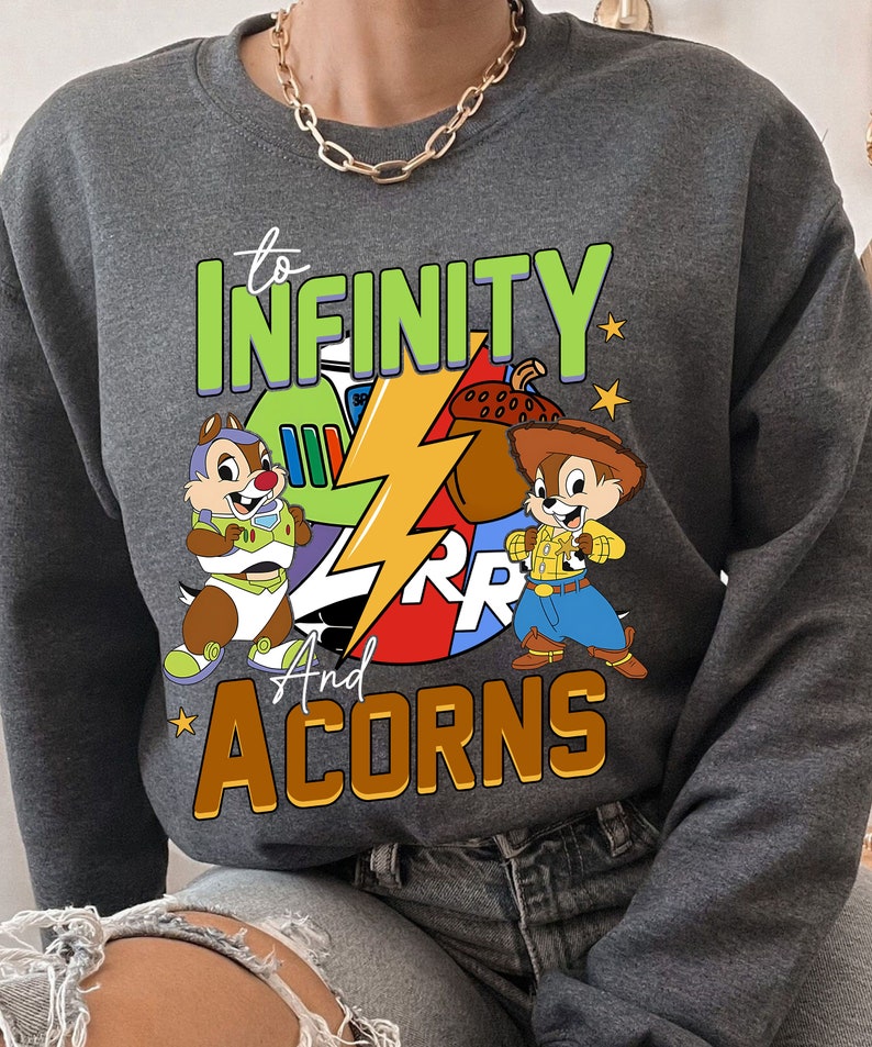 May include: Grey sweatshirt featuring a cartoon graphic of two chipmunks, one dressed as a space ranger and the other as a cowboy. The text "to infinity and acorns" is printed on the sweatshirt.