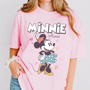 Puede incluir: Camiseta rosa con un gr&aacute;fico de Minnie Mouse con un vestido de lunares. El texto "MINNIE Mouse" est&aacute; impreso encima de ella.