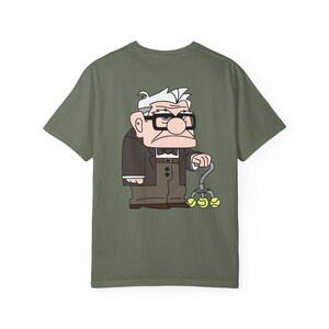 May include: Olive green t-shirt featuring a cartoon illustration of an elderly man with glasses, a suit, and a cane with tennis balls. The character is from the animated movie "Up".