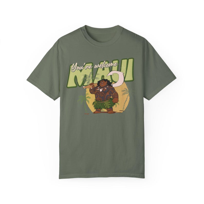 Puede incluir: Una camiseta verde con una imagen de dibujos animados de Maui de la pel&iacute;cula Moana. El texto "You're welcome Maui" est&aacute; impreso en la camiseta.
