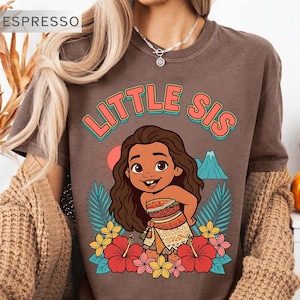 May include: Espresso-colored t-shirt with the text "LITTLE SIS" in coral and teal. The shirt features a cartoon illustration of a girl surrounded by flowers, palm leaves, a mountain, and a sun.