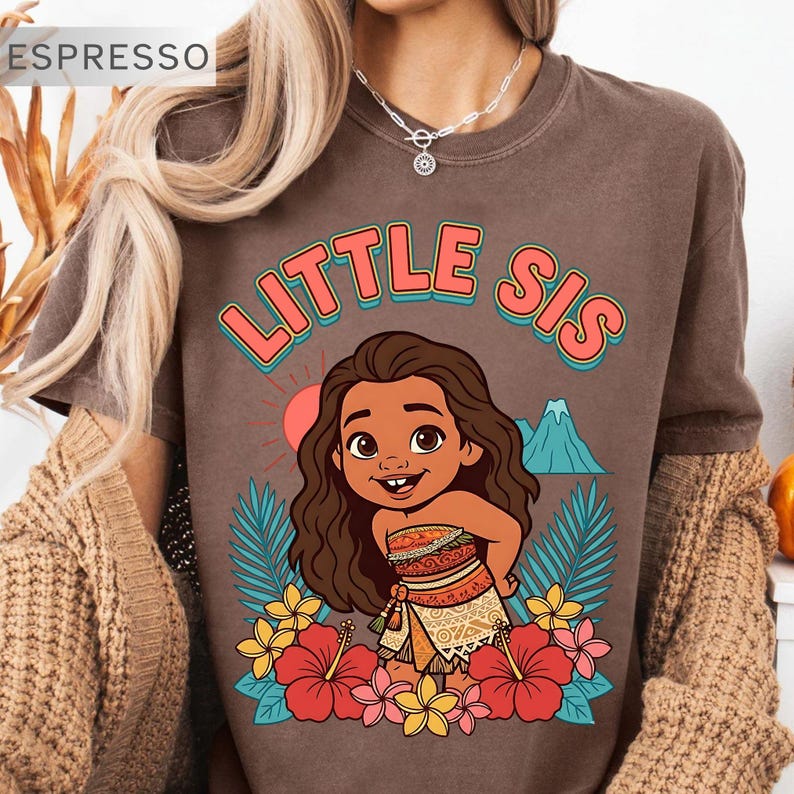May include: Espresso-colored t-shirt with the text "LITTLE SIS" in coral and teal. The shirt features a cartoon illustration of a girl surrounded by flowers, palm leaves, a mountain, and a sun.