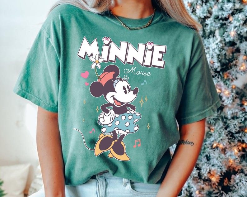 Puede incluir: Una camiseta verde con un gr&aacute;fico de Minnie Mouse con un vestido de lunares. El texto "Minnie Mouse" est&aacute; impreso en blanco sobre el gr&aacute;fico.