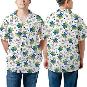 Könnte beinhalten: Ein weißes, kurzärmeliges Hemd mit Knöpfen und einem sich wiederholenden Muster aus grünen Außerirdischen, Planeten und Sternen. Die Außerirdischen tragen blaue Hüte und haben drei Augen.