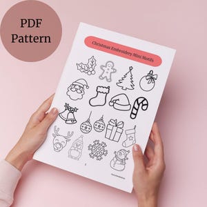 May include: A white PDF pattern sheet featuring Christmas embroidery mini motifs, including a gingerbread man, Christmas tree, Santa Claus, and ornaments. The sheet is held by hands against a pink background. The text "PDF Pattern" is in a pink circle.