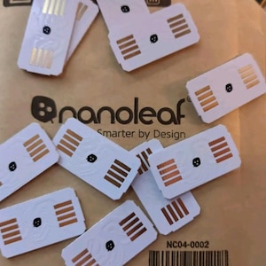 May include: Multiple white rectangular smart home sensors with copper coloured contacts and a small black dot in the centre. The sensors are labelled "nanoleaf" and "Smarter by Design".