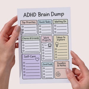 May include: A white ADHD Brain Dump notepad with sections for Top Priorities, Quick Tasks, and more. The notepad has a colorful design with sections for Chores & Errands, Work Projects, and Ideas to Explore. The notepad is held by two hands.