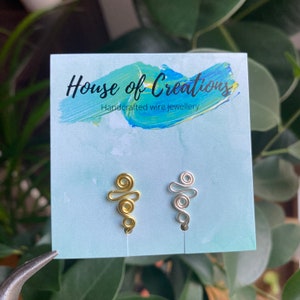 Può includere: Due orecchini in filo metallico fatti a mano, uno dorato e uno argentato, su sfondo blu con il testo "House of Creations Gioielli in filo metallico fatti a mano".