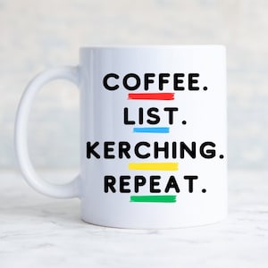 May include: White ceramic coffee mug with black text that reads "COFFEE. LIST. KERCHING. REPEAT." with colored lines under each word.