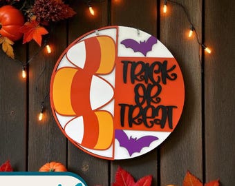 Puede incluir: Un letrero redondo de madera con temática de Halloween. Presenta un diseño de caramelo de maíz a la izquierda y las palabras "Trick or Treat" a la derecha. El letrero tiene detalles en naranja, blanco y morado, con dos siluetas de murciélagos. Fondo de madera.