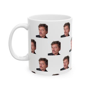May include: White ceramic mug with a repeating pattern of a man's face. The man has dark hair and is wearing a black shirt.