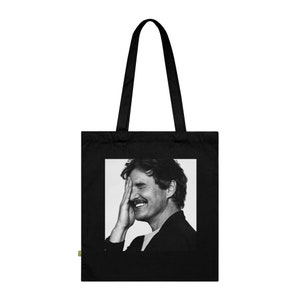 May include: Black tote bag with a black and white photo of a man smiling and covering one eye with his hand.