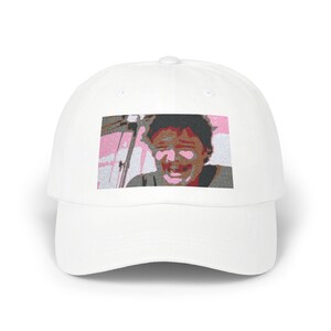 May include: White baseball cap with an embroidered image of a person laughing. The person has brown hair and is wearing a gray shirt. The background is pink and white.